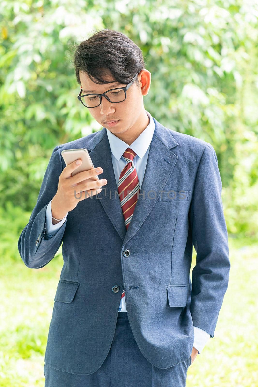 Young asian business men portrait in suit and wear eyeglasses standing outside in a park during sunny day