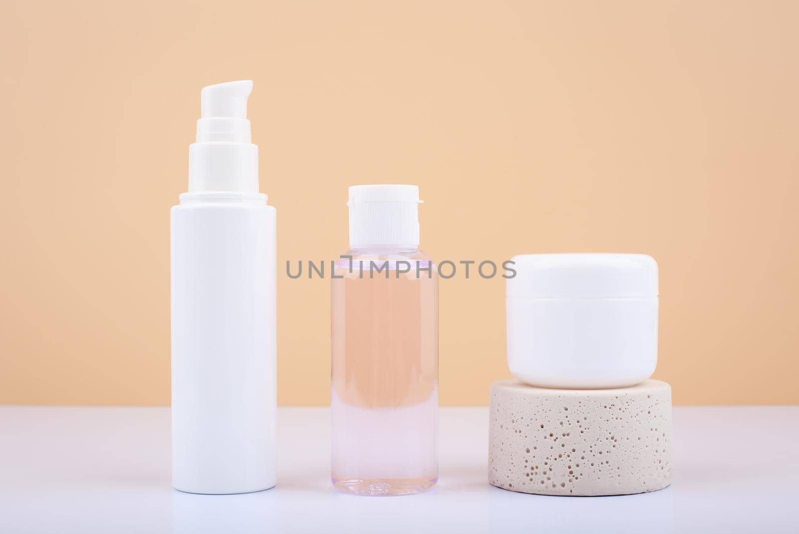 Minimalistic still life with set of cosmetic bottles with face cream, lotion and lip balm on white table against beige background. Concept of healthcare and beauty