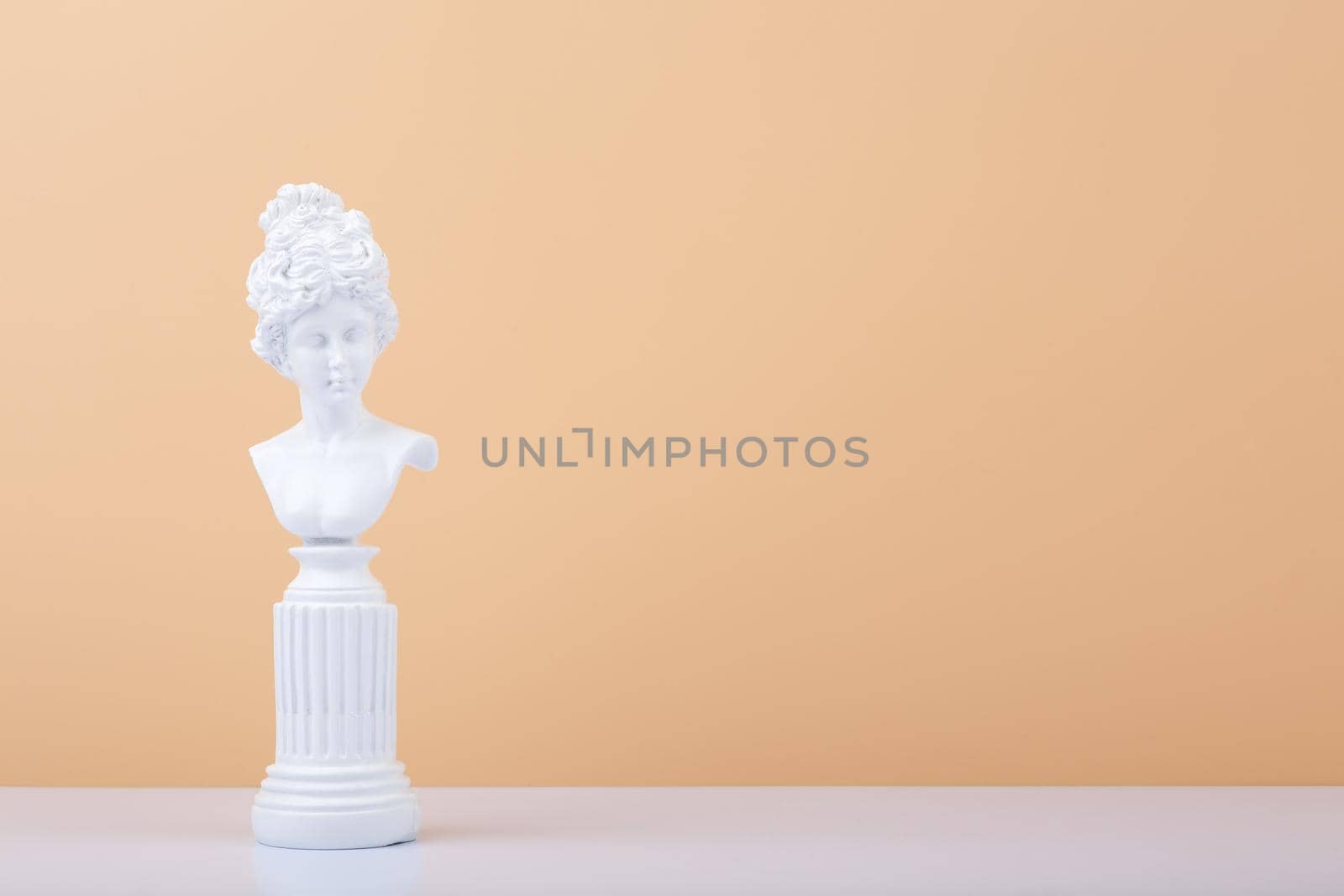White gypsum statue on white table against beige background with copy space. High quality photo