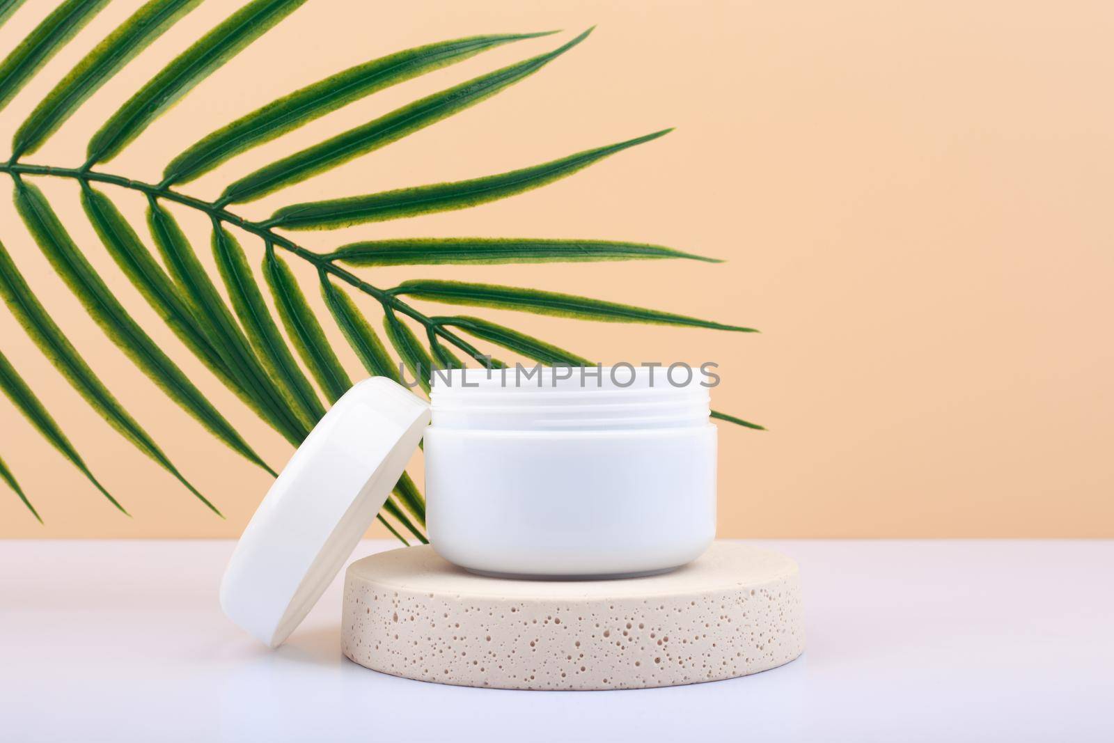 White opened cosmetic jar on beige podium against beige background with palm leaf. Concept of cosmetic products  by Senorina_Irina
