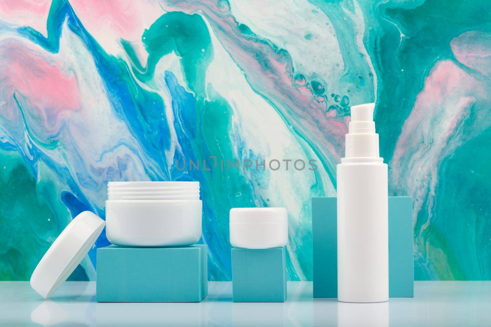 Opened cream jar and set of cosmetic creams for face, neck and under eye area on white table against blue marbled background. Concept of natural organic cosmetics and skin care