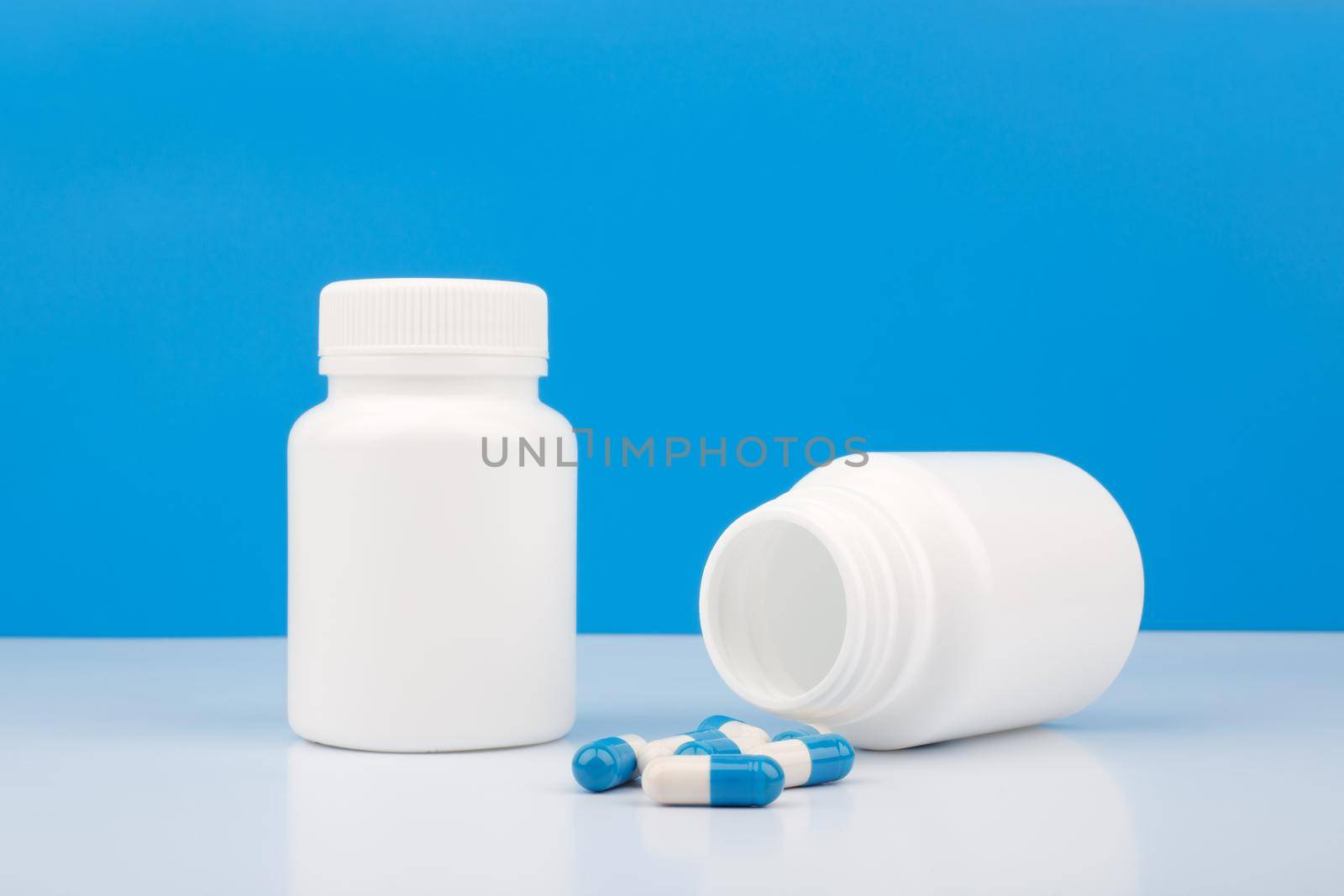 Two bottles with pills against blue background. Close up of medication bottles with spilled pills. Concept of healthcare and medical treatment