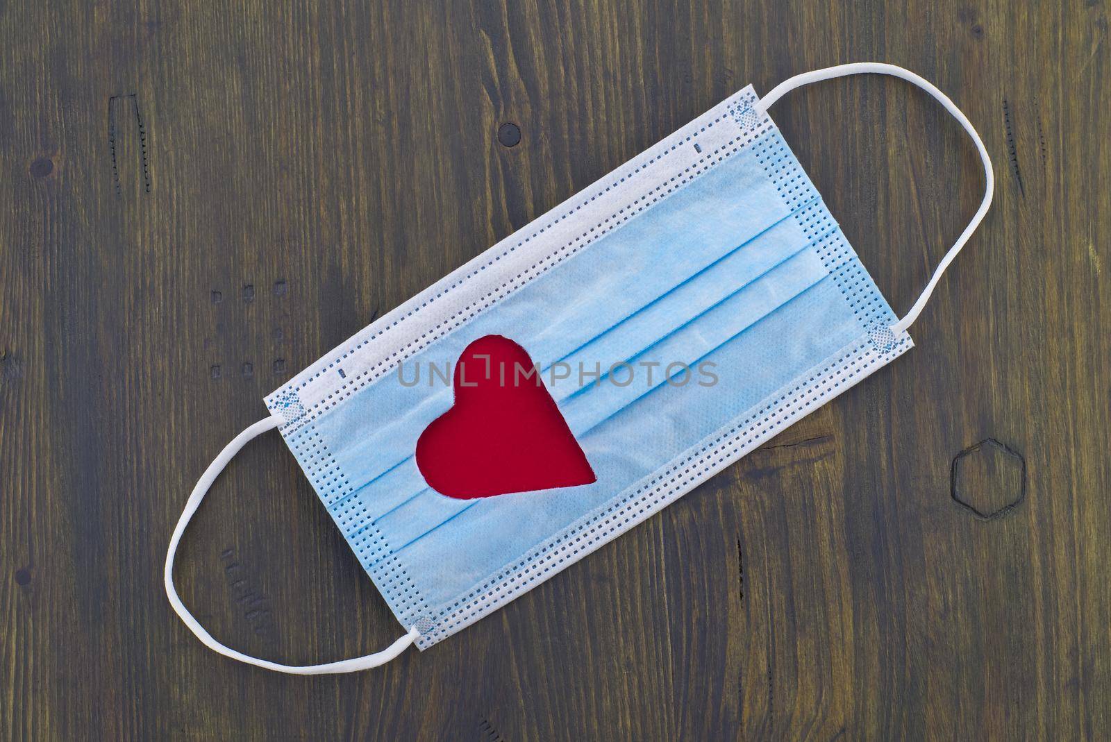 Face mask with a cut-out heart shape over wooden background with free copy space