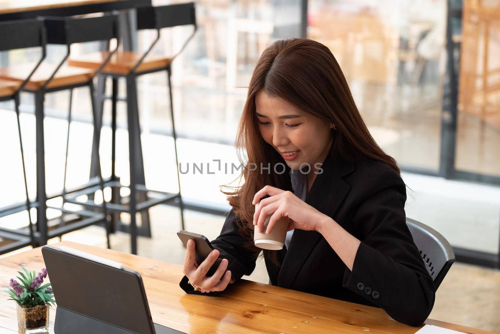 Cropped shot of female business holding cup and using smartphone on wooden table in cafe. by nateemee