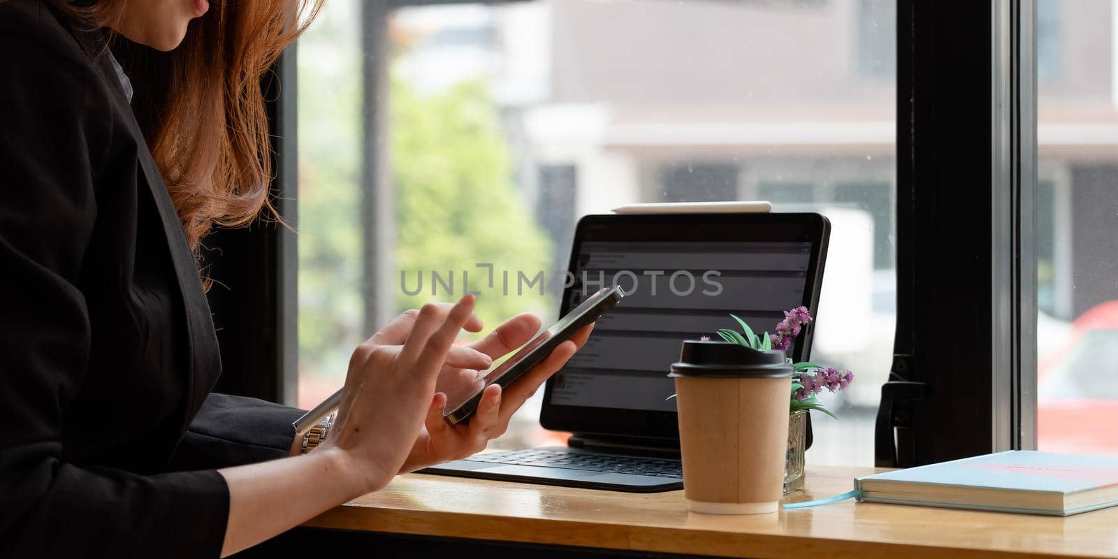 Close up of female hands using modern smart phone while working at office with computer, businesswoman typing text message on her cellphone