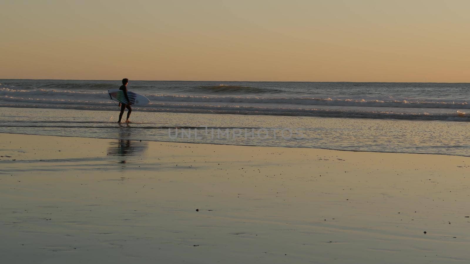 Oceanside, California USA - 27 Dec 2019: Surfer silhouette, pacific ocean beach in evening, water waves and sunset. Tropical coastline, waterfront vacation resort. People enjoy surfing as sport hobby.