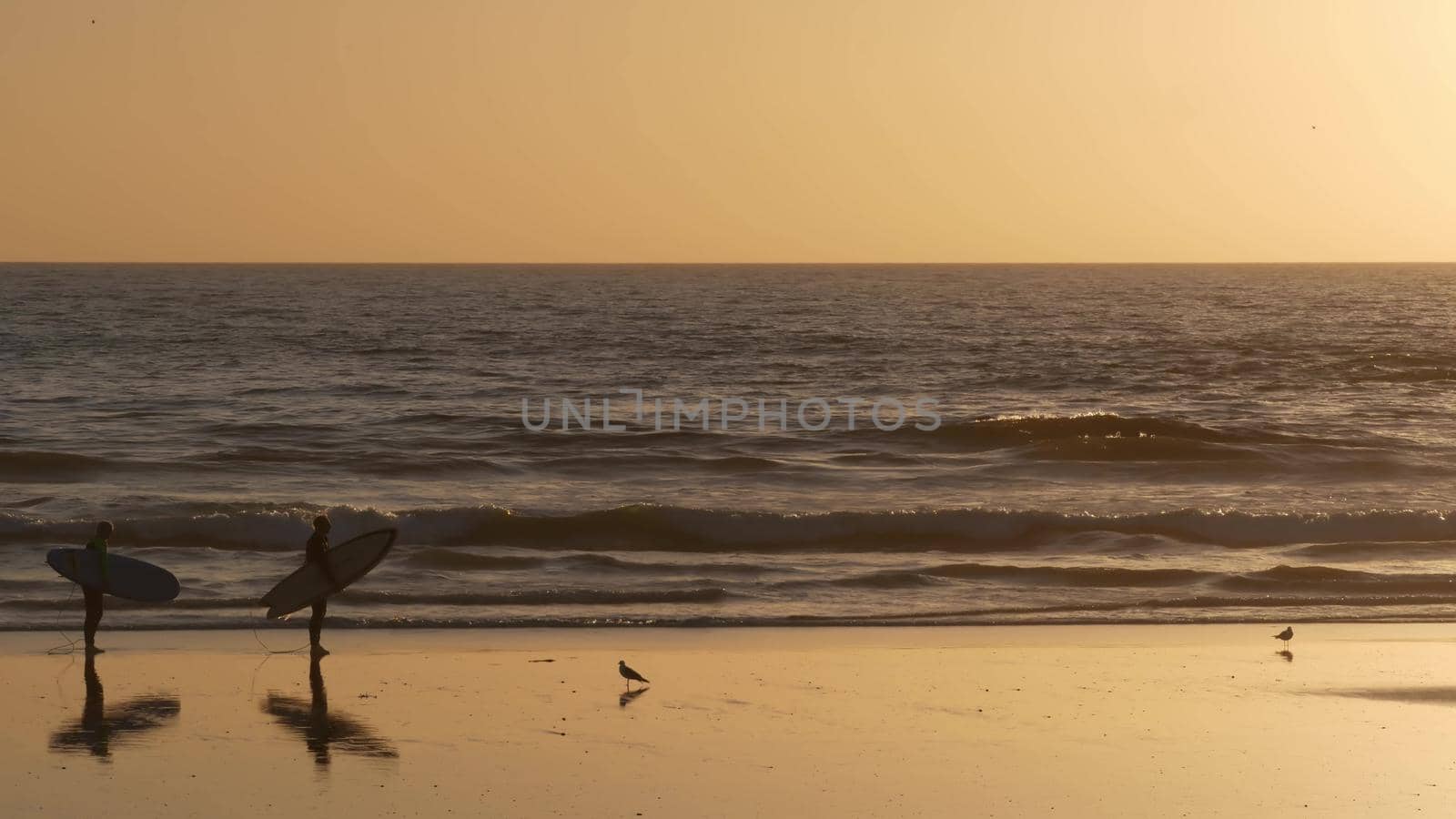 Oceanside, California USA - 11 Feb 2020: Surfer silhouette, pacific ocean beach in evening, water waves and sunset. Tropical coastline, waterfront vacation resort. People enjoy surfing as sport hobby.