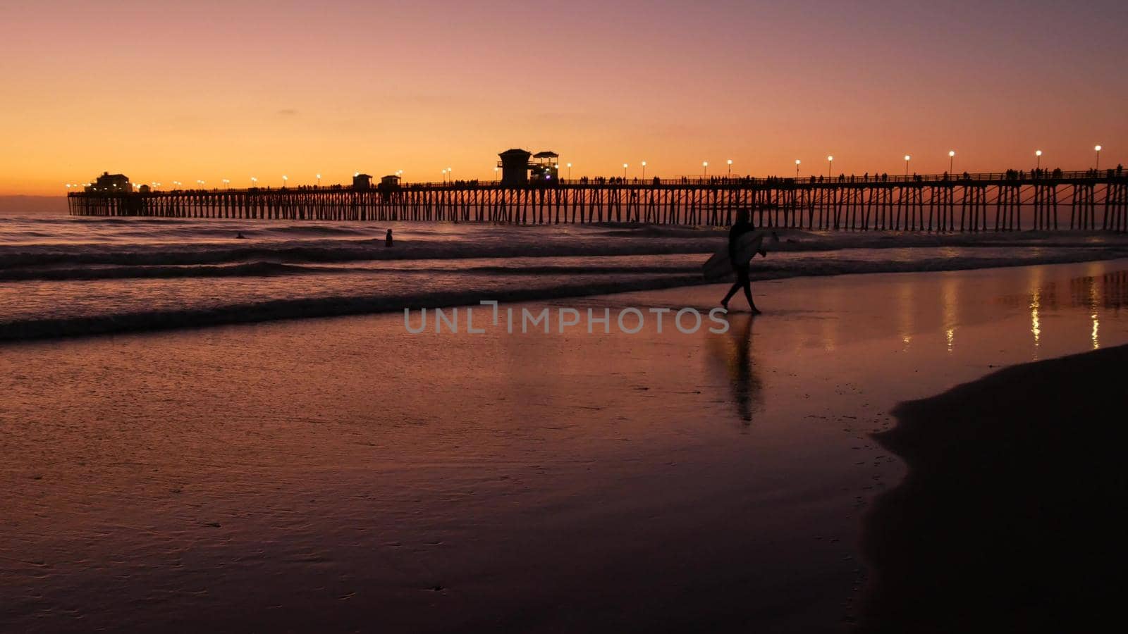 Oceanside, California USA - 16 Feb 2020: Surfer silhouette, pacific ocean beach in evening, water waves and sunset. Tropical coastline, waterfront vacation resort. People enjoy surfing as sport hobby.