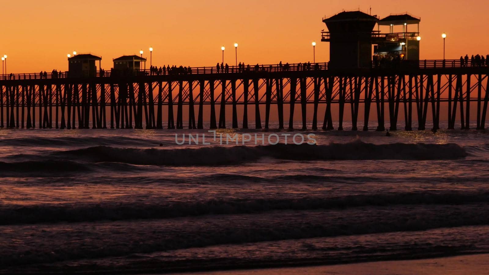 Oceanside, California USA - 16 Feb 2020: Surfer silhouette, pacific ocean beach in evening, water waves and sunset. Tropical coastline, waterfront vacation resort. People enjoy surfing as sport hobby.