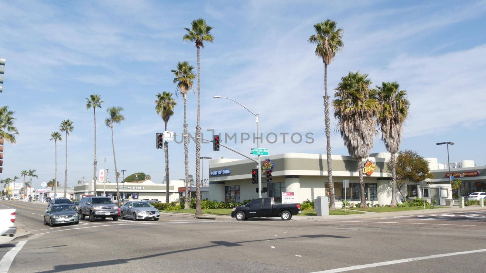 Oceanside, California USA - 27 Jan 2020: Palm trees on Route 101 american highway, pacific coast tropical street. Traffic light and auto transport on road intersection, cars on crossroad in suburb.