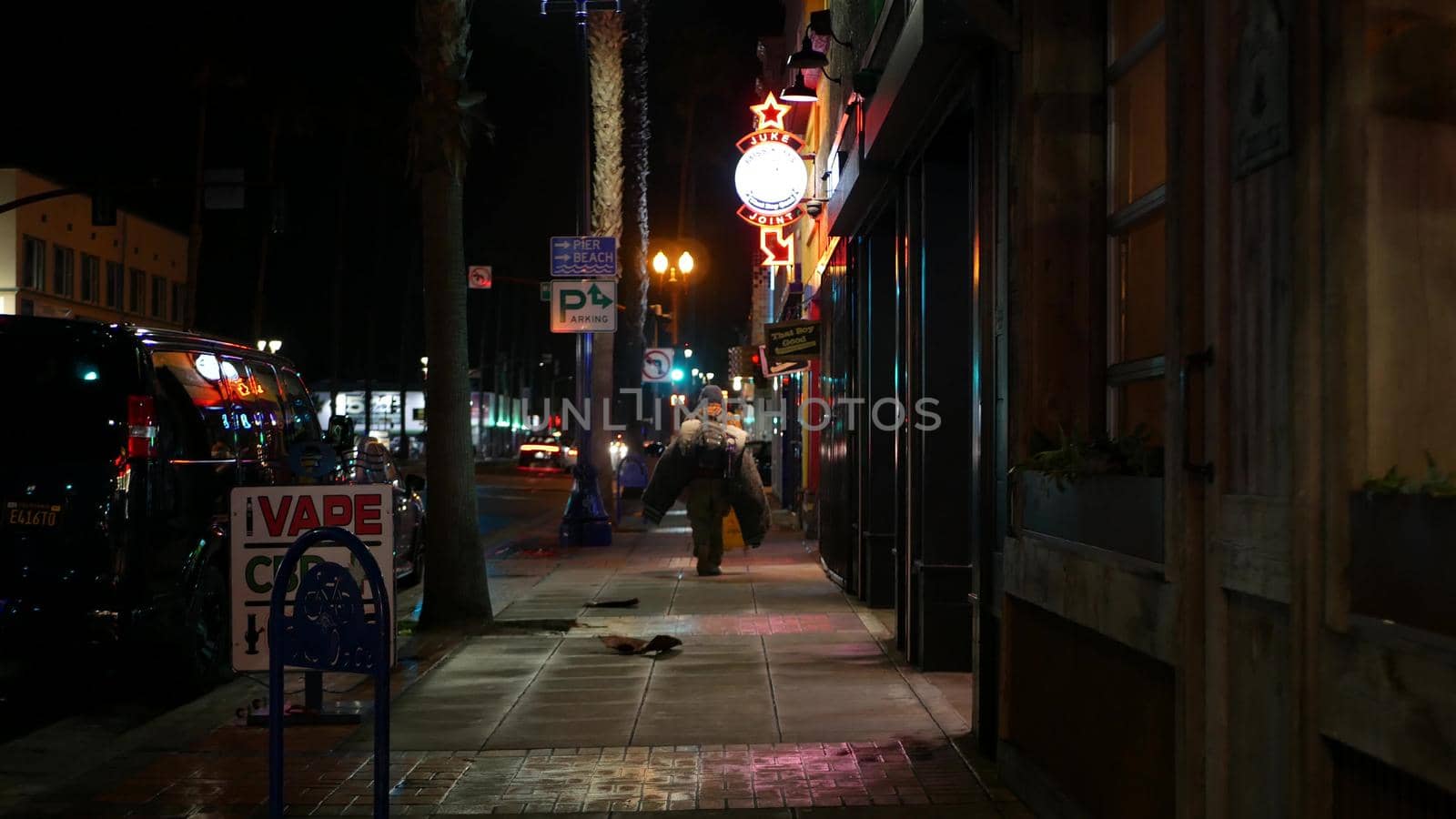 Oceanside, California USA - 9 Feb 2020: Lonely man looks like homeless walking, city street walkway at night. Male person on sidewalk, possible unemployed jobless beggar. Poverty and begging problem.