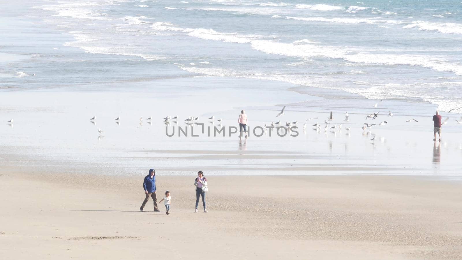 Oceanside, California USA - 11 Feb 2020: Local people walking strolling, pacific ocean coast, beach from pier. Sea water waves tide, shore sand. Beachfront vacations resort. Waterfront promenade.