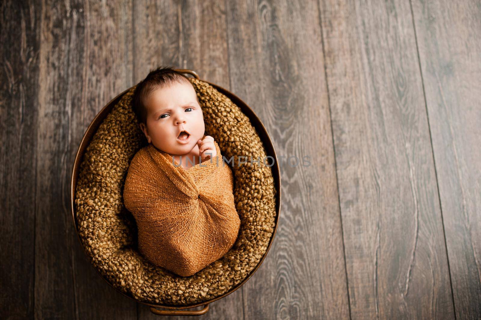 Baby girl in a brown wrap is yawning at a newborn photoshoot. High quality photo