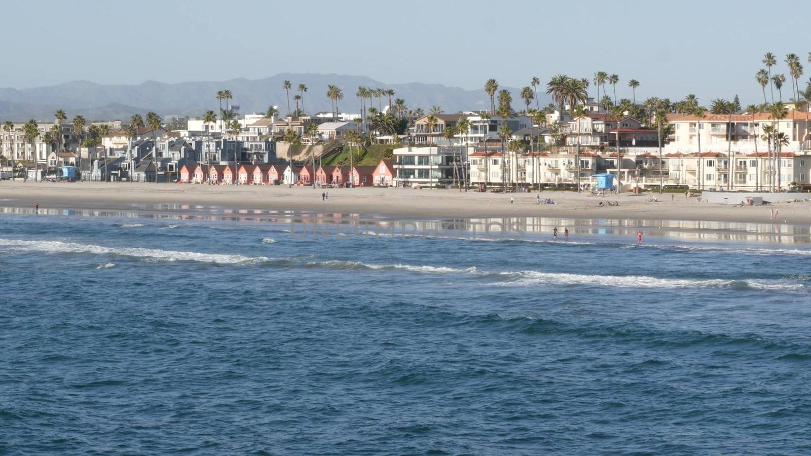 Oceanside, California USA - 11 Feb 2020: Local people walking strolling, pacific ocean coast, beach from pier. Sea water waves tide, shore sand. Beachfront vacations resort. Waterfront promenade.