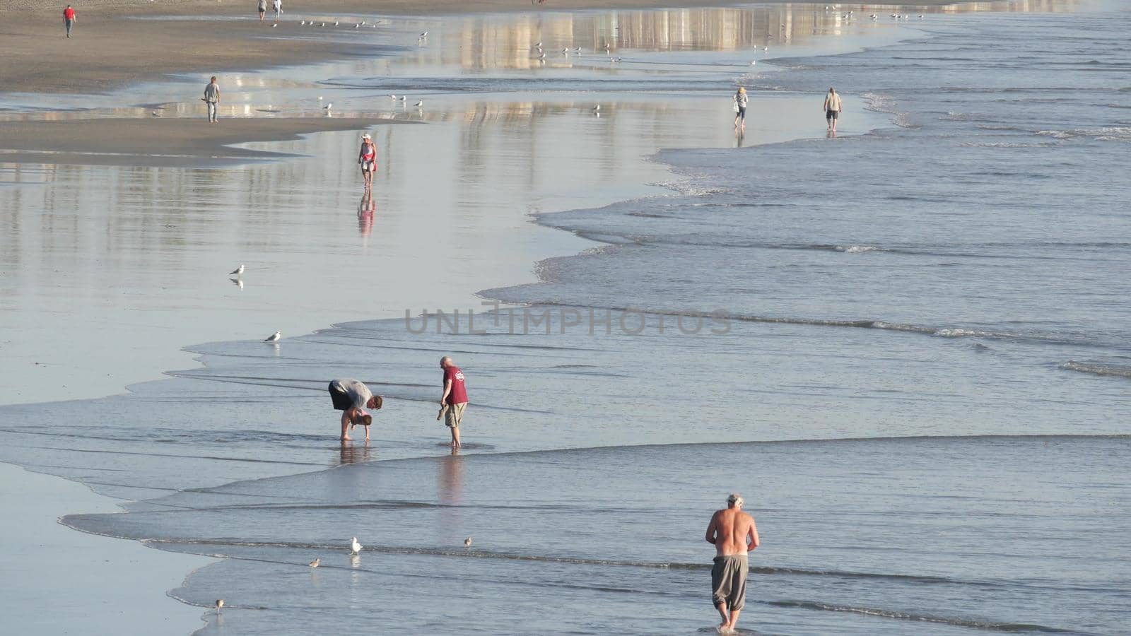 Oceanside, California USA - 11 Feb 2020: Local people walking strolling, pacific ocean coast, beach from pier. Sea water waves tide, shore sand. Beachfront vacations resort. Waterfront promenade.