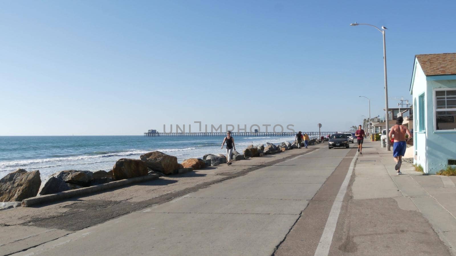 Oceanside, California USA - 16 Feb 2020: People walking strolling on waterfront sea promenade, beachfront boardwalk, pier. Vacations ocean beach resort near Los Angeles. Men running, healthy lifestyle