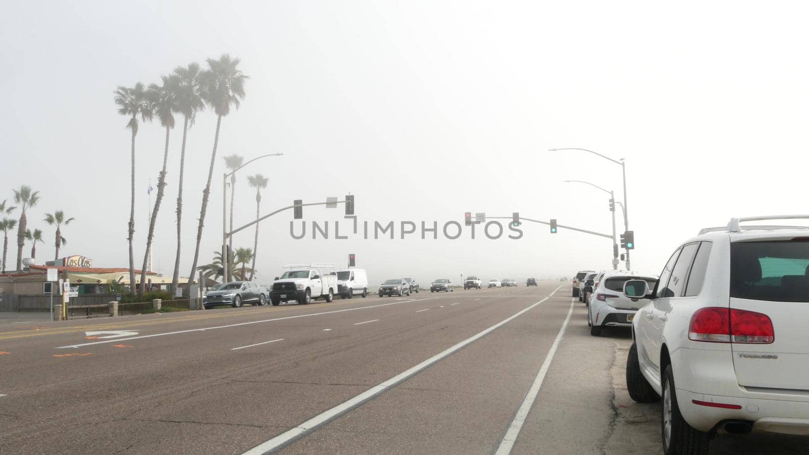 Encinitas, California USA -20 Feb 2020: Traffic light semaphore on highway 101 road by misty beach. Fog on sea shore, pacific ocean coast. Freeway with cars along shoreline, coastline near Los Angeles