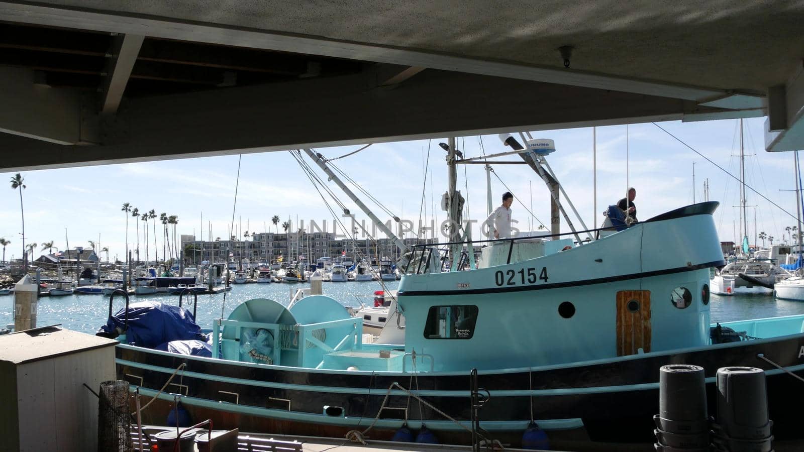 Oceanside, California USA - 26 Feb 2020: Harbor village with fisherman boats and yachts, pacific ocean coast marina, sea shore. Blue nautical vessel for fishing in port, fishery industry. Men working.