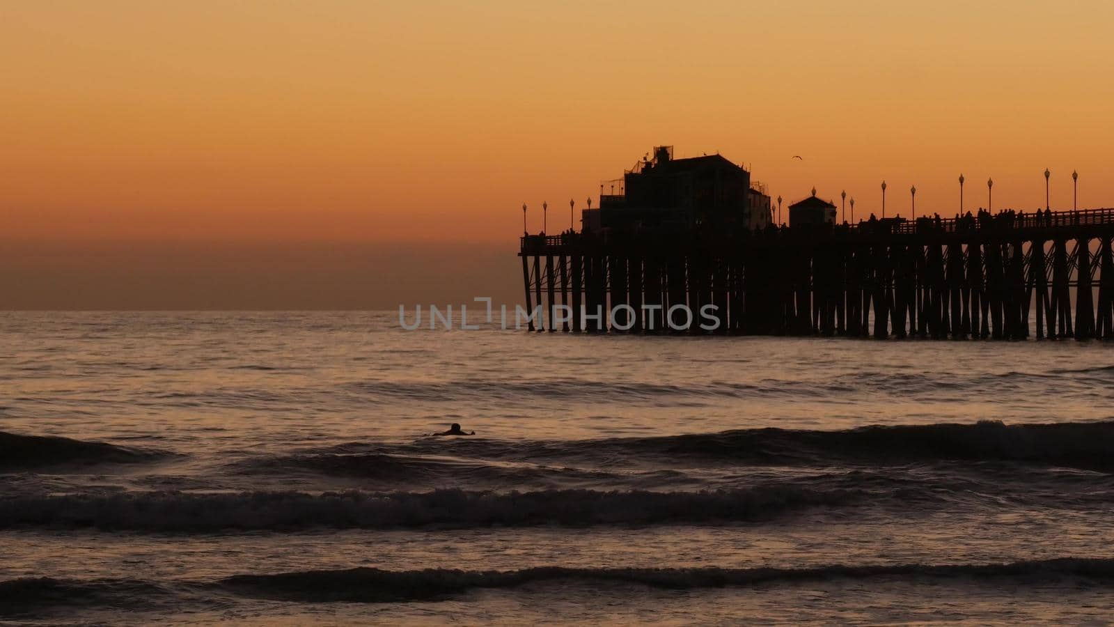 Oceanside, California USA - 16 Feb 2020: Surfer silhouette, pacific ocean beach in evening, water waves and sunset. Tropical coastline, waterfront vacation resort. People enjoy surfing as sport hobby.