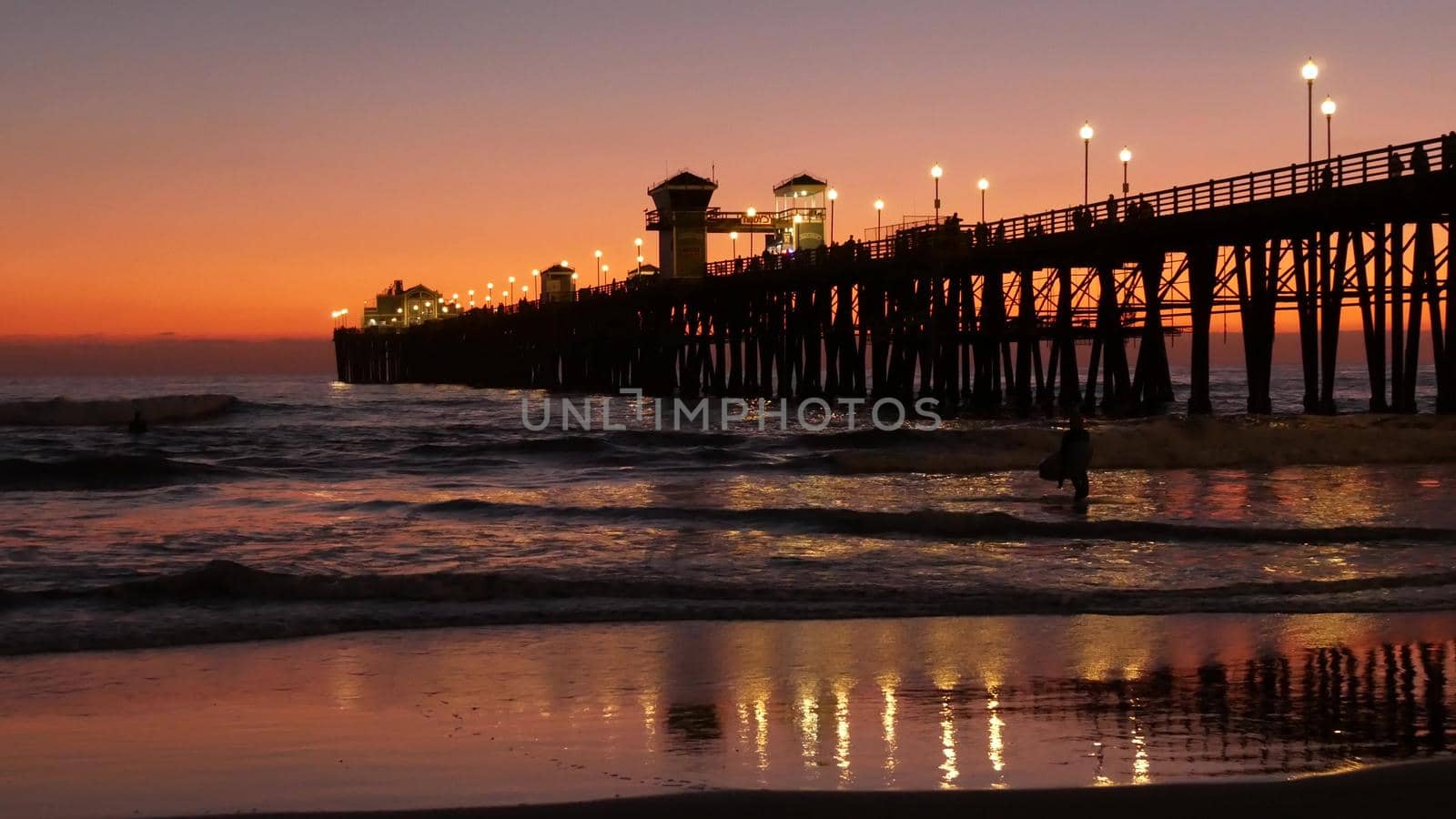 Surfer silhouette, pacific ocean beach sunset. People enjoy surfing. Oceanside, California USA by DogoraSun