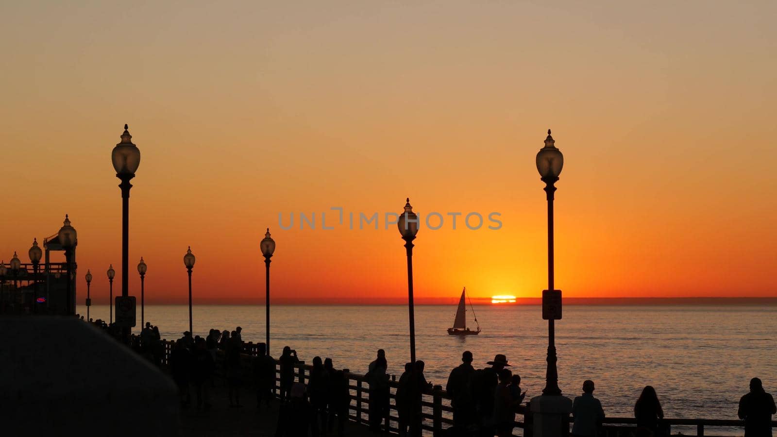 Oceanside, California USA - 17 Nov. 2019: Wooden pier and people walking. Tourists strolling in waterfront resort, summertime vacations near Los Angeles. Sunset ocean beach, tropical sunny orange sky.