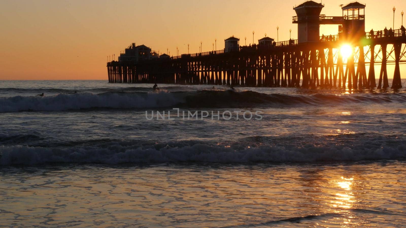 Oceanside, California USA - 16 Feb 2020: Surfer silhouette, pacific ocean beach in evening, water waves and sunset. Tropical coastline, waterfront vacation resort. People enjoy surfing as sport hobby.