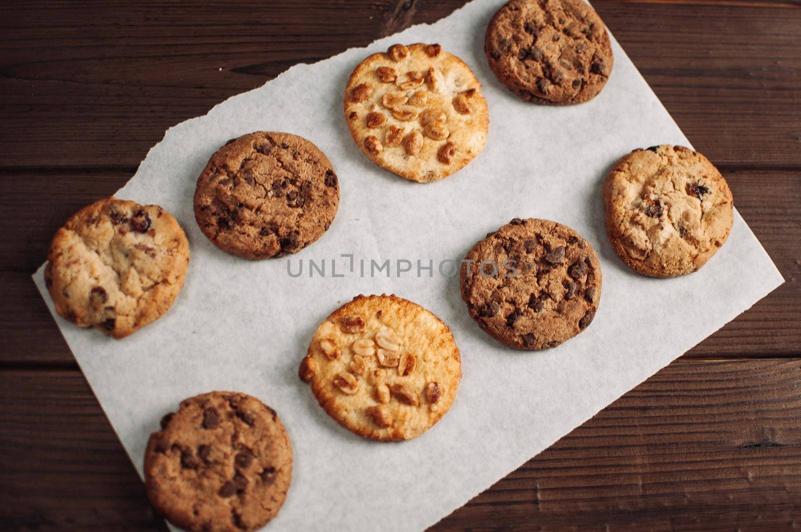 Chocolate covered cookies lay on a parchment paper in a row. Gluten-free cookies on a wooden table out of the oven. Selective focus