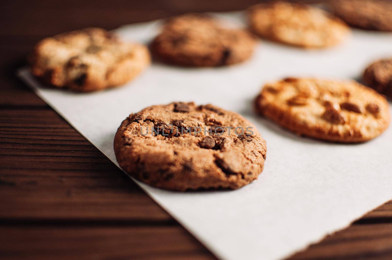 Chocolate covered cookies lay on a parchment paper in a row. Gluten-free cookies on a wooden table out of the oven. Selective focus