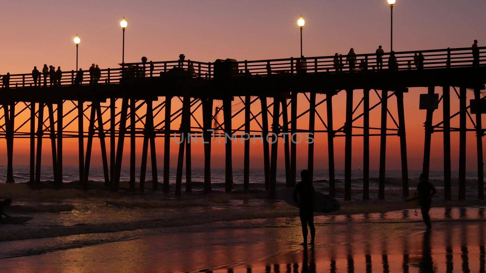 Surfer silhouette, pacific ocean beach sunset. People enjoy surfing. Oceanside, California USA by DogoraSun