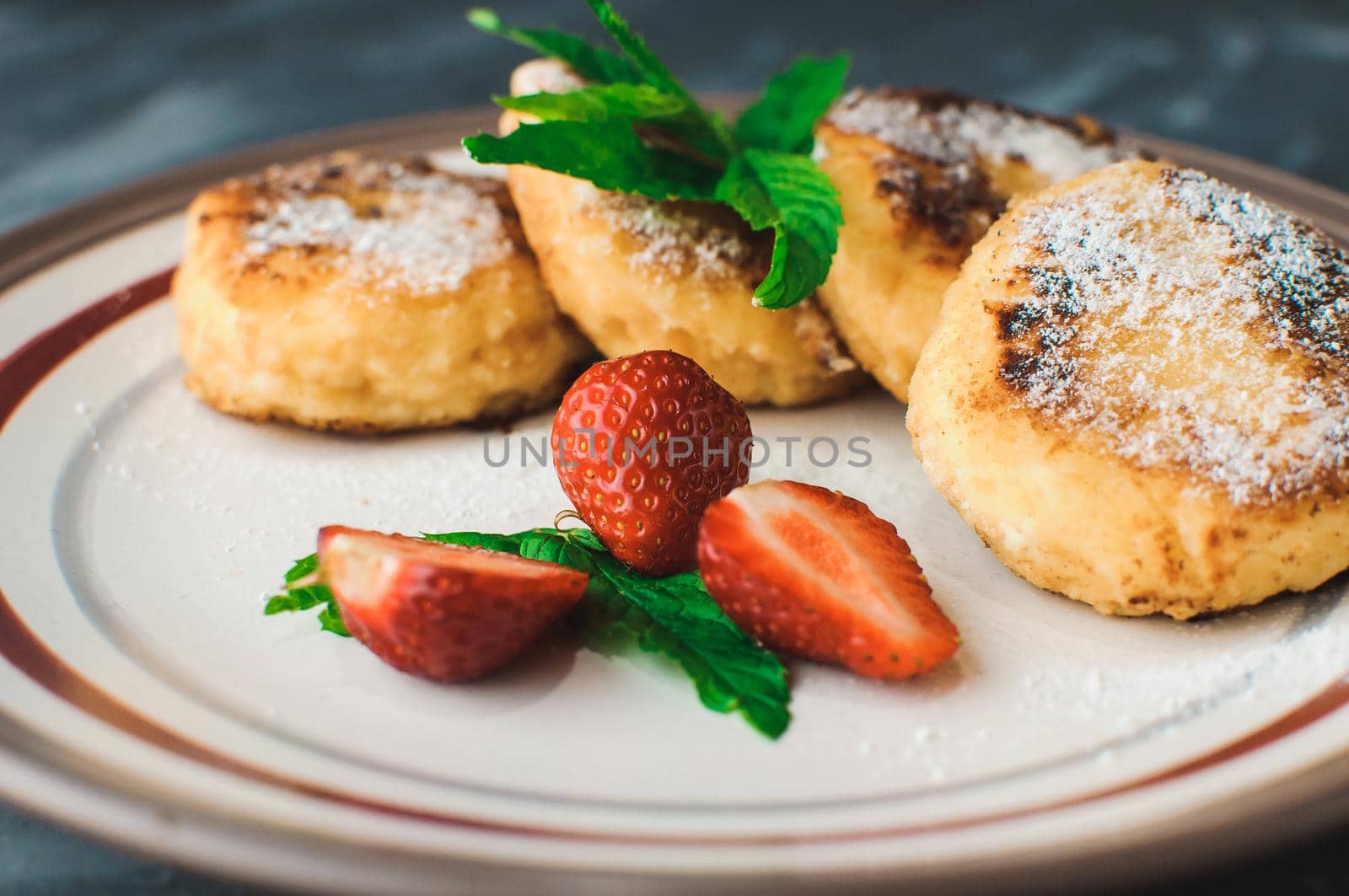 Gourmet breakfast - curd pancakes, cheesecakes, curd pancakes with strawberries, mint and icing sugar in a white plate. Selective focus.