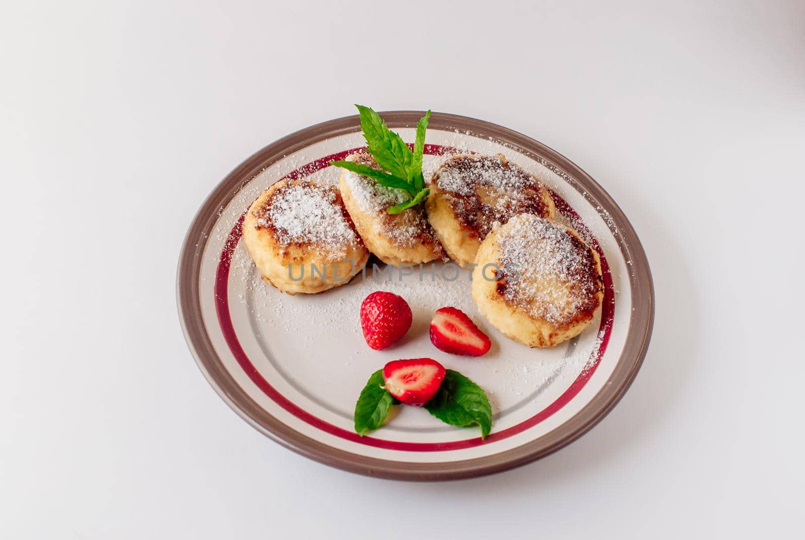 Gourmet breakfast - cottage cheese pancakes, cheesecakes, cottage cheese pancakes with strawberries, mint and powdered sugar in a white plate. Useful dessert on white background isolate