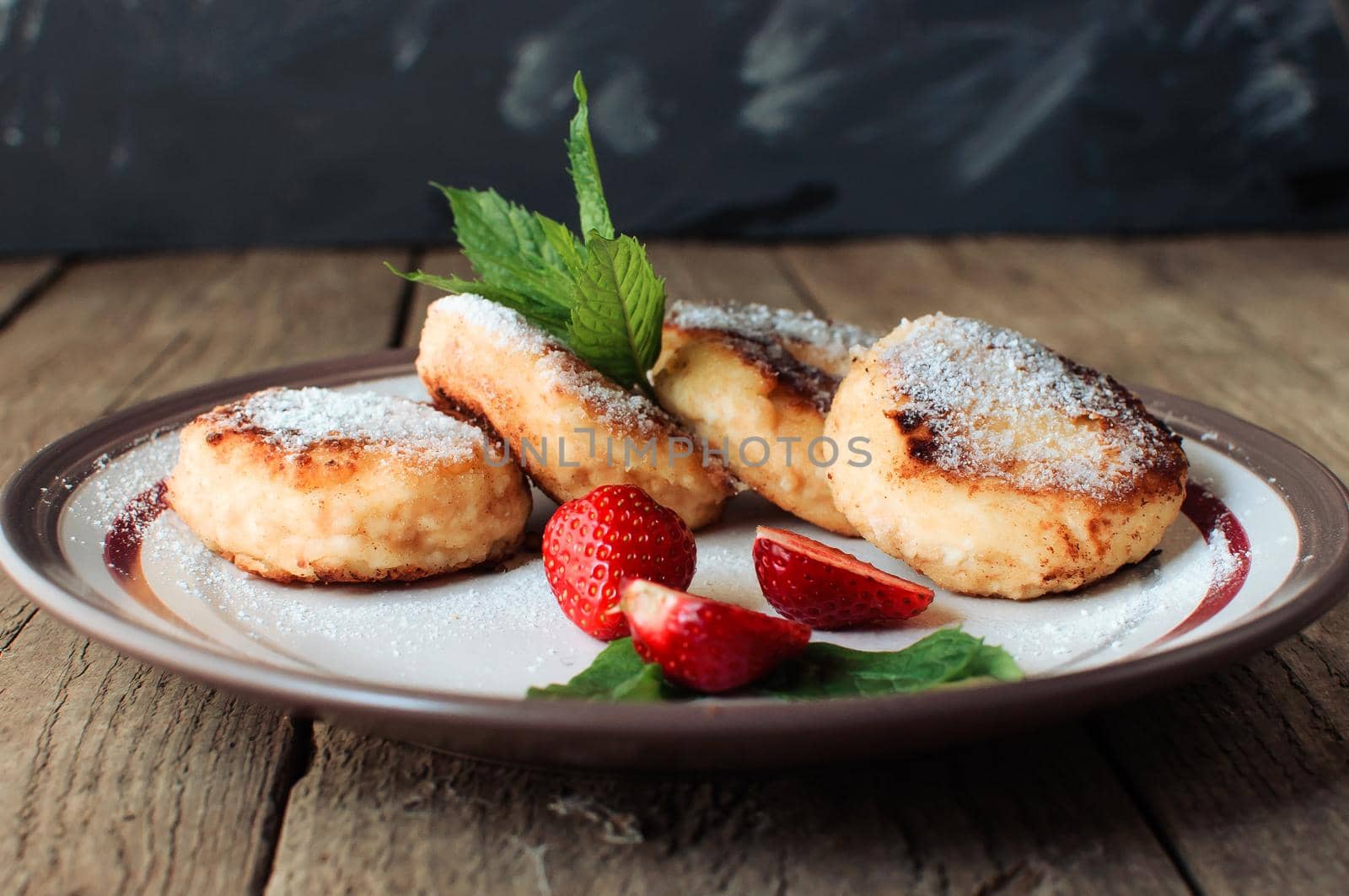 Gourmet breakfast - cottage cheese pancakes, cheesecakes, cottage cheese pancakes with strawberries, mint and powdered sugar in a white plate. Selective focus.