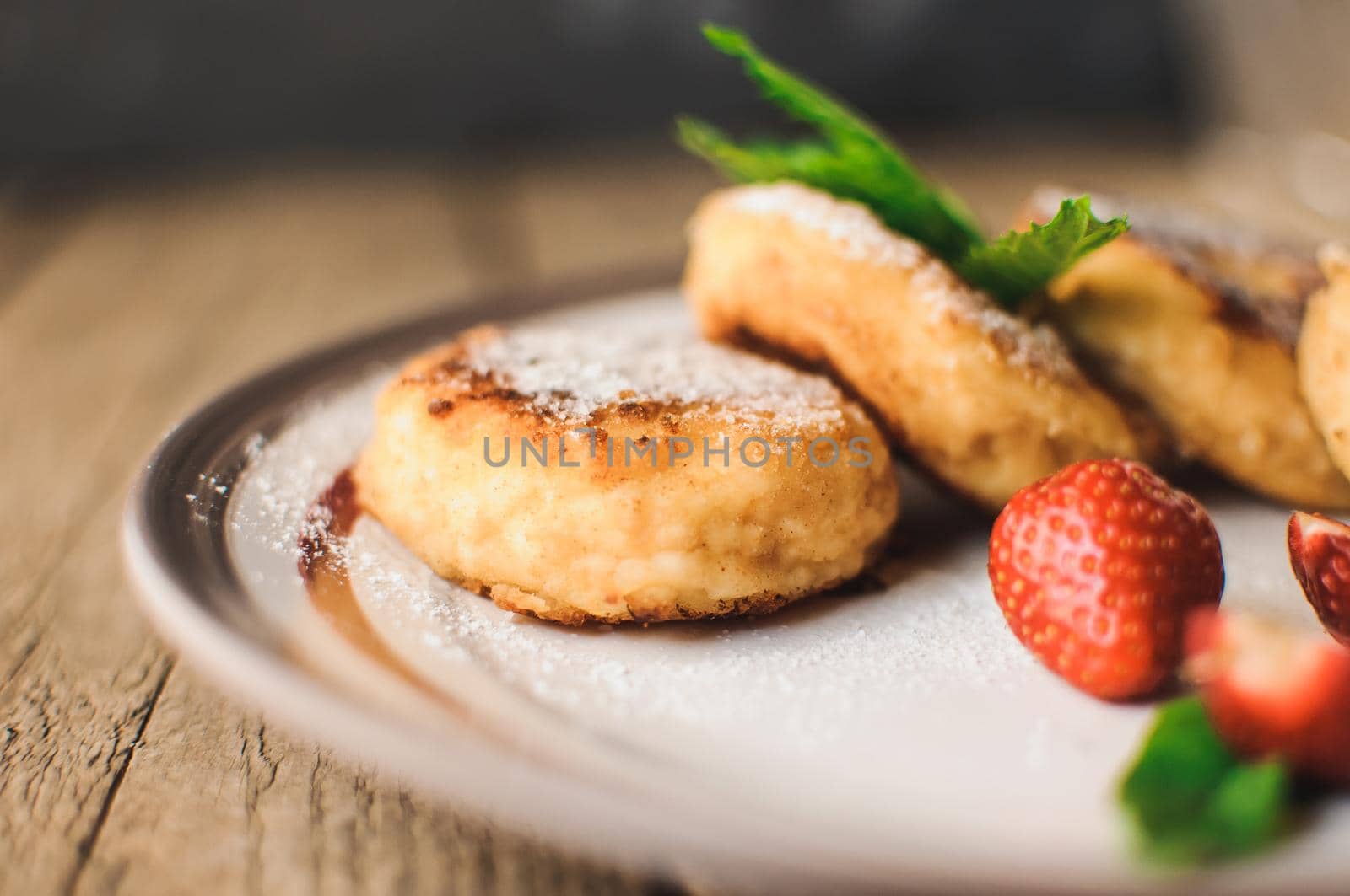 Gourmet breakfast - cottage cheese pancakes, cheesecakes, cottage cheese pancakes with strawberries, mint and powdered sugar in a white plate. Selective focus.