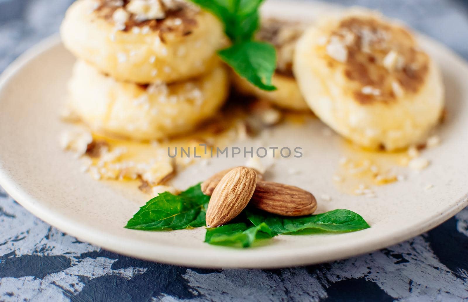 Cheesecakes, cottage cheese pancakes with almonds, fresh mint and maple syrup on a gray background from a concrete table. Cheesecakes, homemade traditional Ukrainian and Russian cheesecakes, top view.