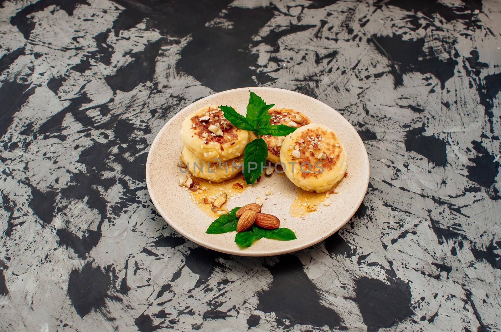 Cheesecakes, cottage cheese pancakes with almonds, fresh mint and maple syrup on a gray background from a concrete table. Cheesecakes, homemade traditional Ukrainian and Russian cheesecakes
