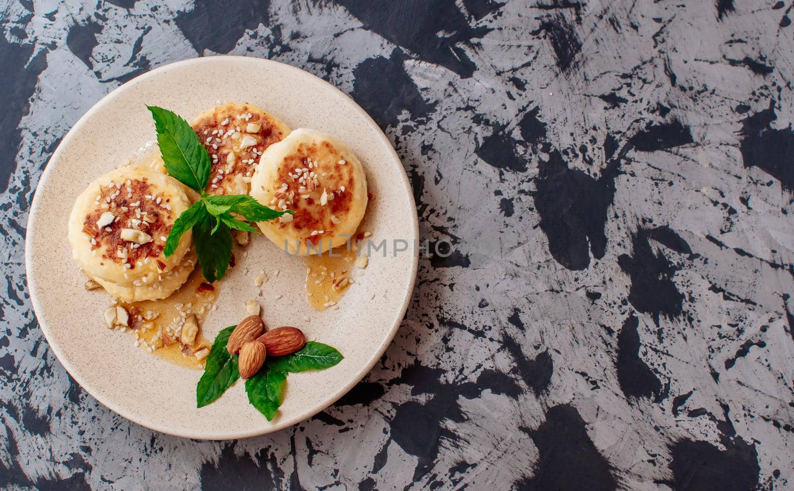 Cheesecakes,cottage cheese pancakes with almonds,fresh mint and maple syrup on a gray background from a concrete table copy space. Cheesecakes, homemade traditional Ukrainian and Russian cheesecakes