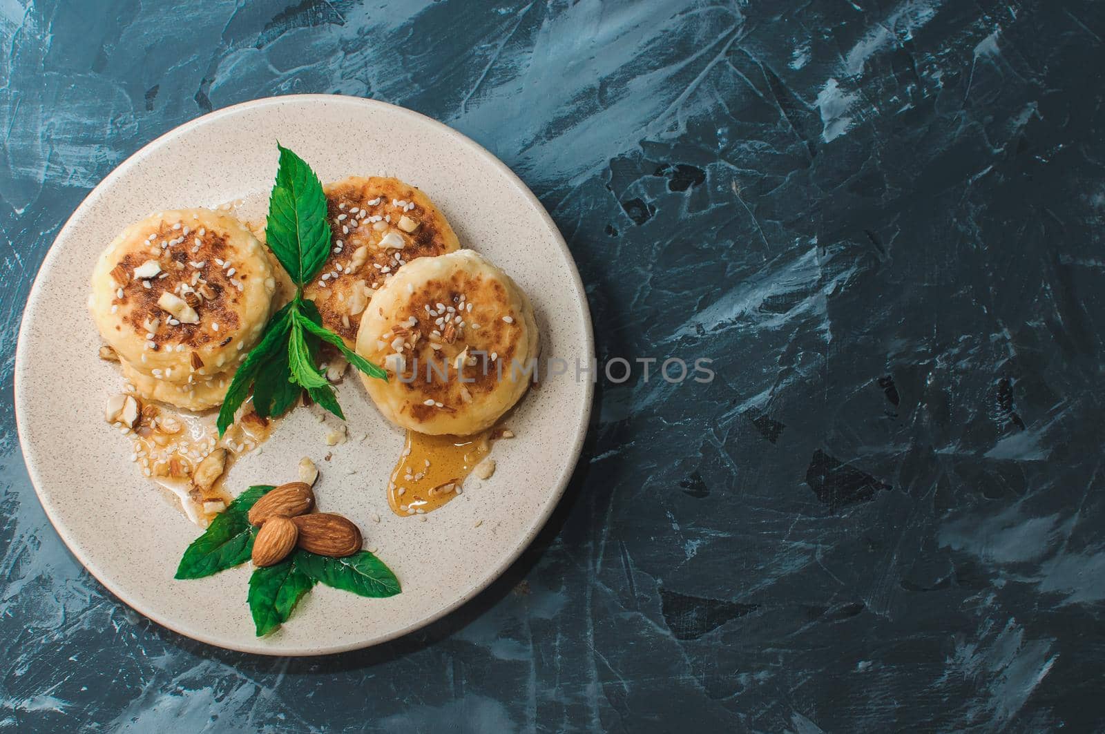 Cheesecakes,cottage cheese pancakes with almonds,fresh mint and maple syrup on a gray background from a concrete table copy space. Cheesecakes, homemade traditional Ukrainian and Russian cheesecakes