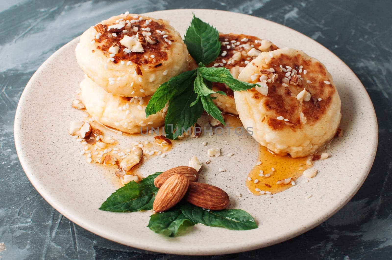 Cheesecakes,cottage cheese pancakes with almonds,fresh mint and maple syrup on a gray background from a concrete table. Cheesecakes, homemade traditional Ukrainian and Russian cheesecakes