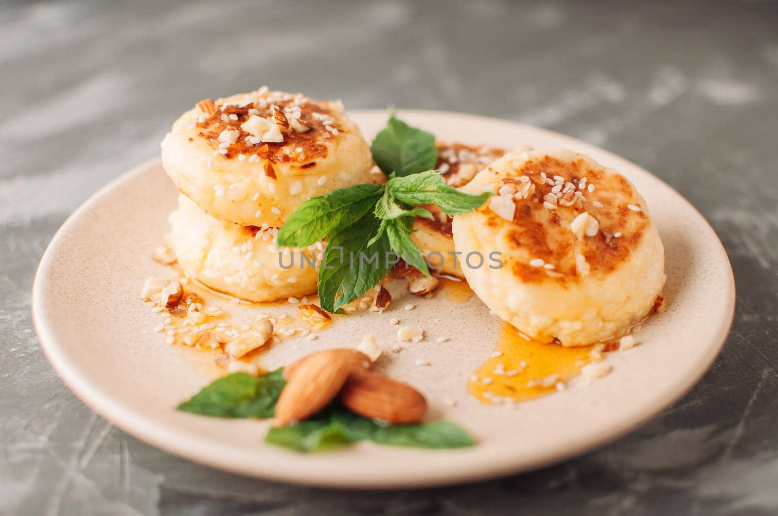 Cheesecakes,cottage cheese pancakes with almonds,fresh mint and maple syrup on a gray background from a concrete table. Cheesecakes, homemade traditional Ukrainian and Russian cheesecakes