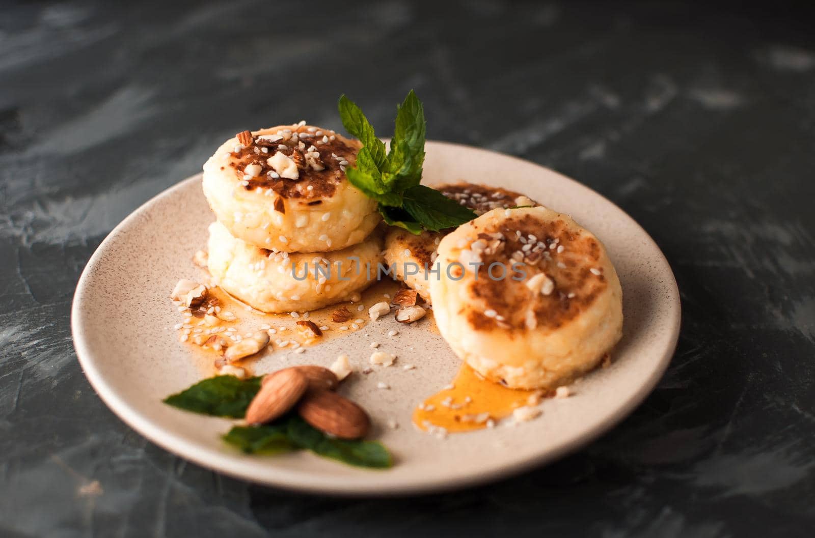 Cheesecakes,cottage cheese pancakes with almonds,fresh mint and maple syrup on a gray background from a concrete table. Cheesecakes, homemade traditional Ukrainian and Russian cheesecakes