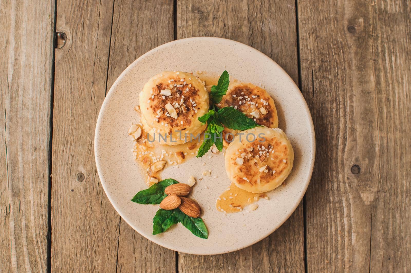 Delicious breakfast - cottage cheese pancakes,cheesecakes, cottage cheese pancakes with almonds, mint and maple syrup in a beige plate.Useful dessert on a wooden table in rustic style.Selective focus.