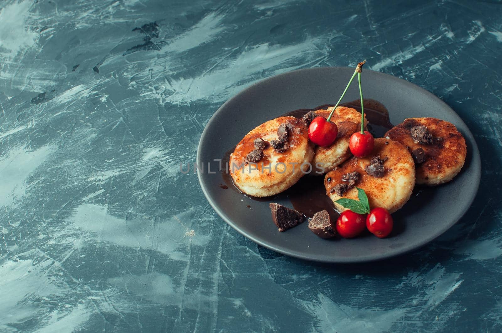 Breakfast Food Tasty Concept. Cheesecakes, cheesecakes, cottage cheese pancakes with cherries and chocolate on a black background concrete table. Close-up.Healthy food