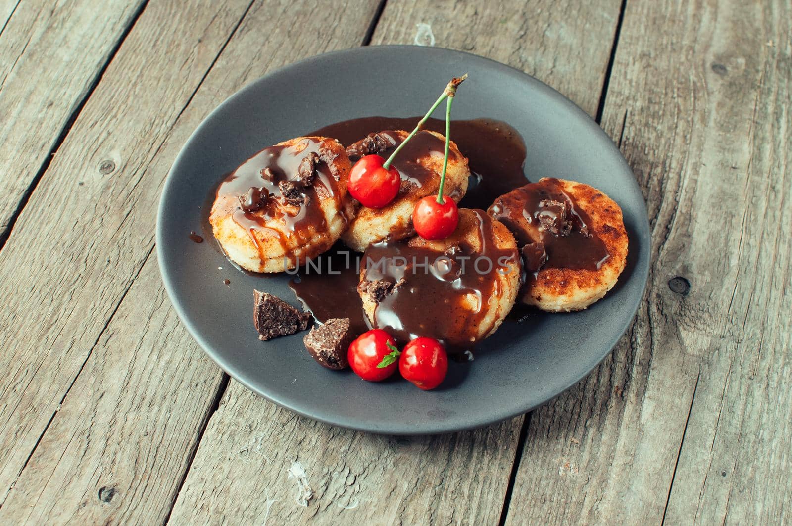 Gourmet breakfast - curd pancakes, cheesecakes, curd pancakes with cherries and chocolate in a brown plate. Wholesome dessert on a wooden table in a rustic style. Selective focus