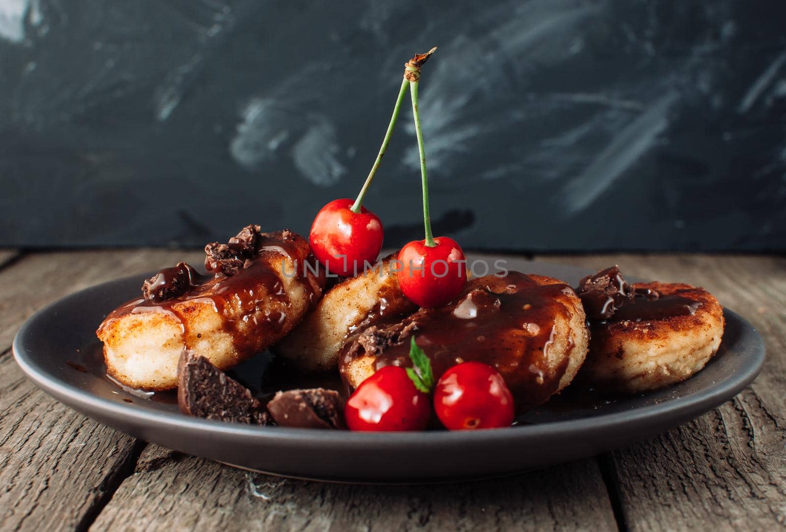 Gourmet breakfast - curd pancakes, cheesecakes, curd pancakes with cherries and chocolate in a brown plate. Wholesome dessert on a wooden table in a rustic style. Selective focus