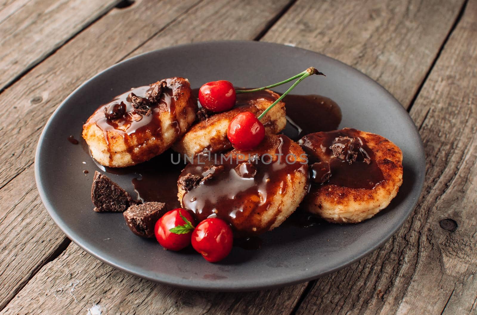 Gourmet breakfast - curd pancakes, cheesecakes, curd pancakes with cherries and chocolate in a brown plate. Wholesome dessert on a wooden table in a rustic style. Selective focus