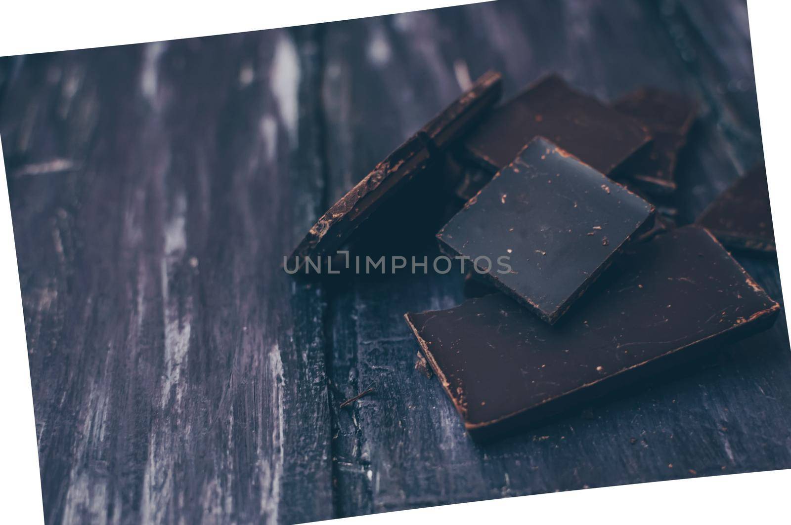 dark chocolate without sugar and gluten free for diabetics and allergics. Pieces of chocolate on a dark rustic table. Photo in a white frame at an angle. Copy space