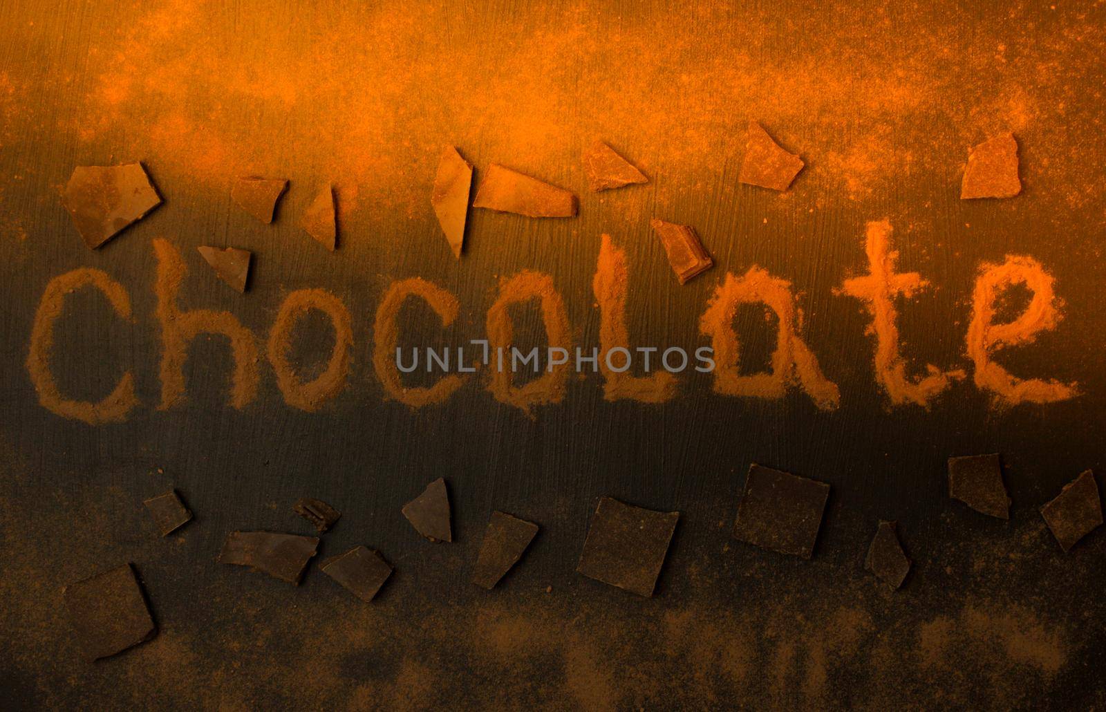 inscription chocolate made of cocoa powder with the addition of pieces of chocolate and chocolate powder on a black graphite background with a sunbeam