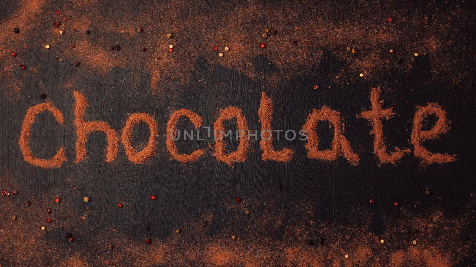 inscription chocolate made of cocoa powder with the addition of pieces of chocolate, chocolate powder, red, black and white pepper on a black graphite background