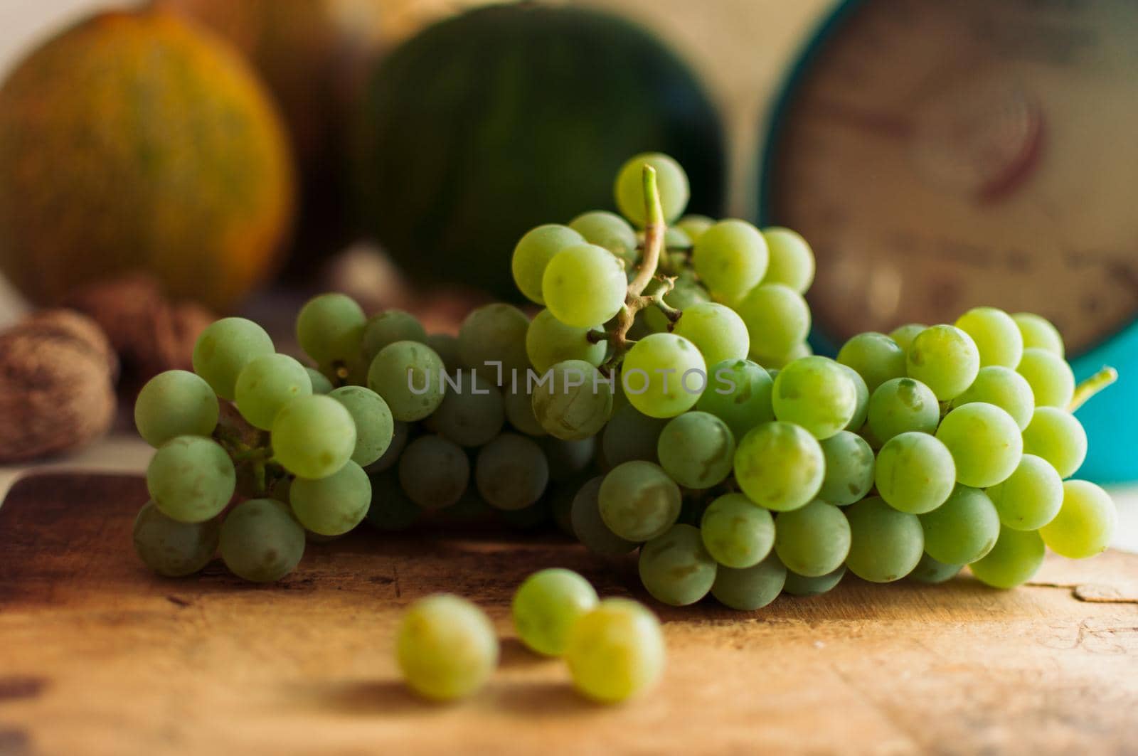 Autumn still life.Green grapes lie on wooden board.In the background are pumpkins,walnuts and scales.Autumn harvest concept.Happy Thanksgiving.Selective focus.Horizontal orientation.