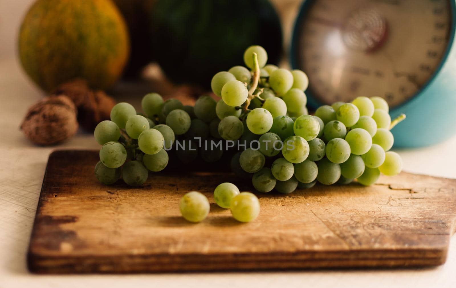 Autumn still life.Green grapes lie on wooden board.In the background are pumpkins,walnuts and scales.Autumn harvest concept.Happy Thanksgiving.Selective focus.Horizontal orientation.
